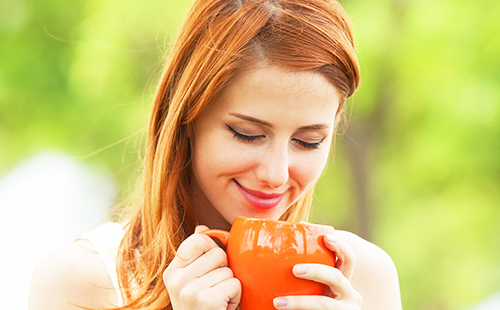 Рыжая девушка пьёт отвар из большой оранжевой чашки